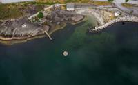 Et dronebilde av Kråkeskarvetstranda, som viser badeplattformen i fjorden, stupebrett, garderobebygg og strandområdet.