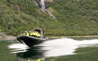 En ribbåt fylt med passasjerer i fart langs fjorden.