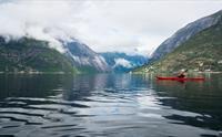 En kvinne i rød kajakk padler på fjorden, med Simadal i bakgrunnen.
