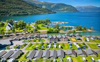 Luftfoto av Mikkelparken Ferietun i Kinsarvik, omgitt av Hardangerfjorden og majestetiske fjell. Perfekt feriestad for heile familien.
