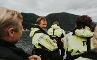 Smilande turistar på båttur i Hardangerfjorden omgitt av vakre fjell.