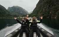 Glade turistar løftar armane i glede medan dei køyrer gjennom fjorden i Hardanger.