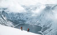 To skigåere ved et vann omringet av snøkledde fjell.