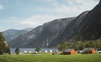 Sæbø camping sett fra hovedveien, med vann og fjell i bakgrunnen.