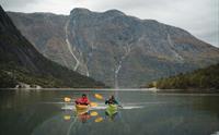 Et par padler kajakk på fjorden med et høyt fjell i bakgrunnen.