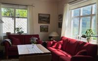 Lyst og innbydande opphaldsrom på Jaastad Gjestetun med raude sofaer, naturlege detaljar og utsyn til Hardanger-naturen.