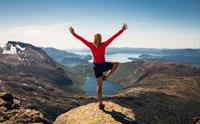 Kvinne står og poserer og ser utover panoramautsikt mot fjord og fjell.