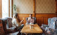 To venninner sit i ei sjarmerande stove på Thon Hotel Sandven og nyt eit glas fersk juice, omgitt av tradisjonell norsk interiørstil.