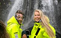 Smilande passasjerar i gule redningsdrakter nyt ei frisk oppleving under ein foss på RIB-safari i Hardanger.