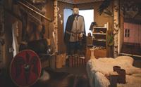 Inne i vikingutstillingen, et skjold, en utstillingsdukke iført vikingeklær, en seng med saueskinn, et reinsdyrskinn hengende på veggen.