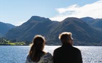 Eit par ser utover Hardangerfjorden og fjella frå Hardangerfjordekspressen.