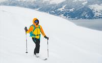 En oransje og gulkledd person på ski på topptur i Hardanger.