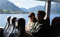 Eit par sit innandørs på Hardangerfjordekspressen og nyt utsikta over fjorden gjennom store vindauge.