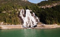 Furubergsfossen frå fjorden – Eit storslått bilete av Furubergsfossen som renn nedover klippene ved fjorden i Kvinnherad, omgitt av frodig natur.