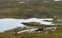 En kvinnelig turgåer som står på en høyde og ser ned på Halne Fjellstugu.