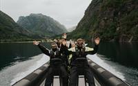 Glade passasjerar på ribbåt som vinkar medan dei reiser gjennom det vakre landskapet i Hardanger.