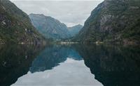 Spegelblank Hardangerfjord omgitt av bratte fjell og grøne åsar.