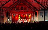 Band playing on stage with audience. Red stage lights.