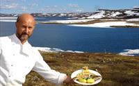 Kokken holder en tallerken med fjellørret, med Halnesjøen i bakgrunnen.