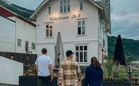 Tre personar går mot Siderhuset Ola K, ein idyllisk restaurant i Hardanger, omgitt av fjord og fjell.