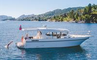 Båten Pilagutt i Hardangerfjorden med sol, blått vatn og folk som badar. Perfekt for ein avslappande fjordcruiseoppleving.