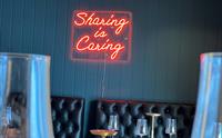"Sharing is Caring" neonskilt på veggen i UNI Sushi & Izakaya.