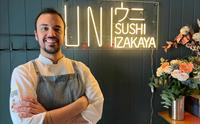 Smilende kokk foran UNI Sushi & Izakaya neon-skiltet.
